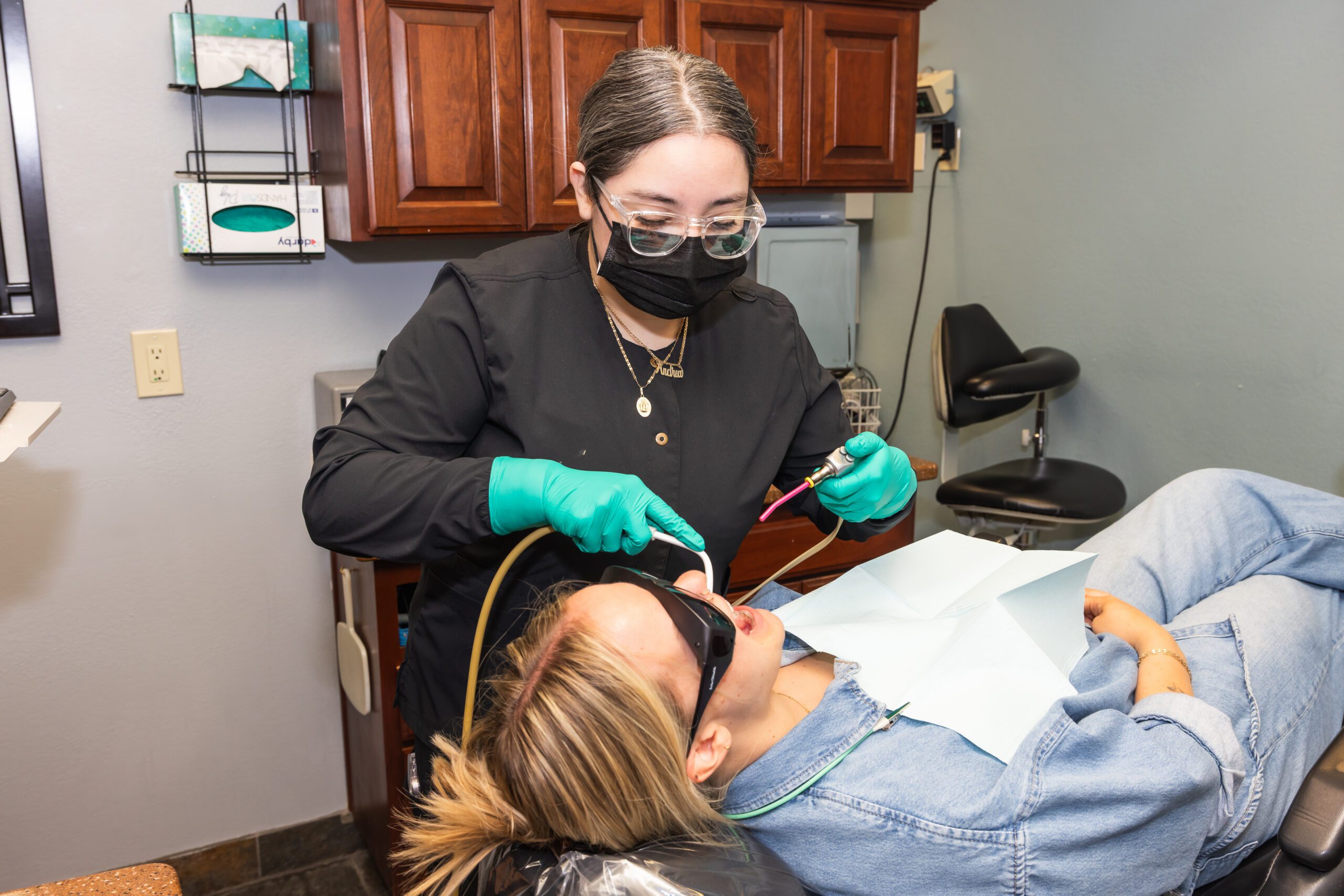 Staff in black scrubs and mask, examining a patient's teeth