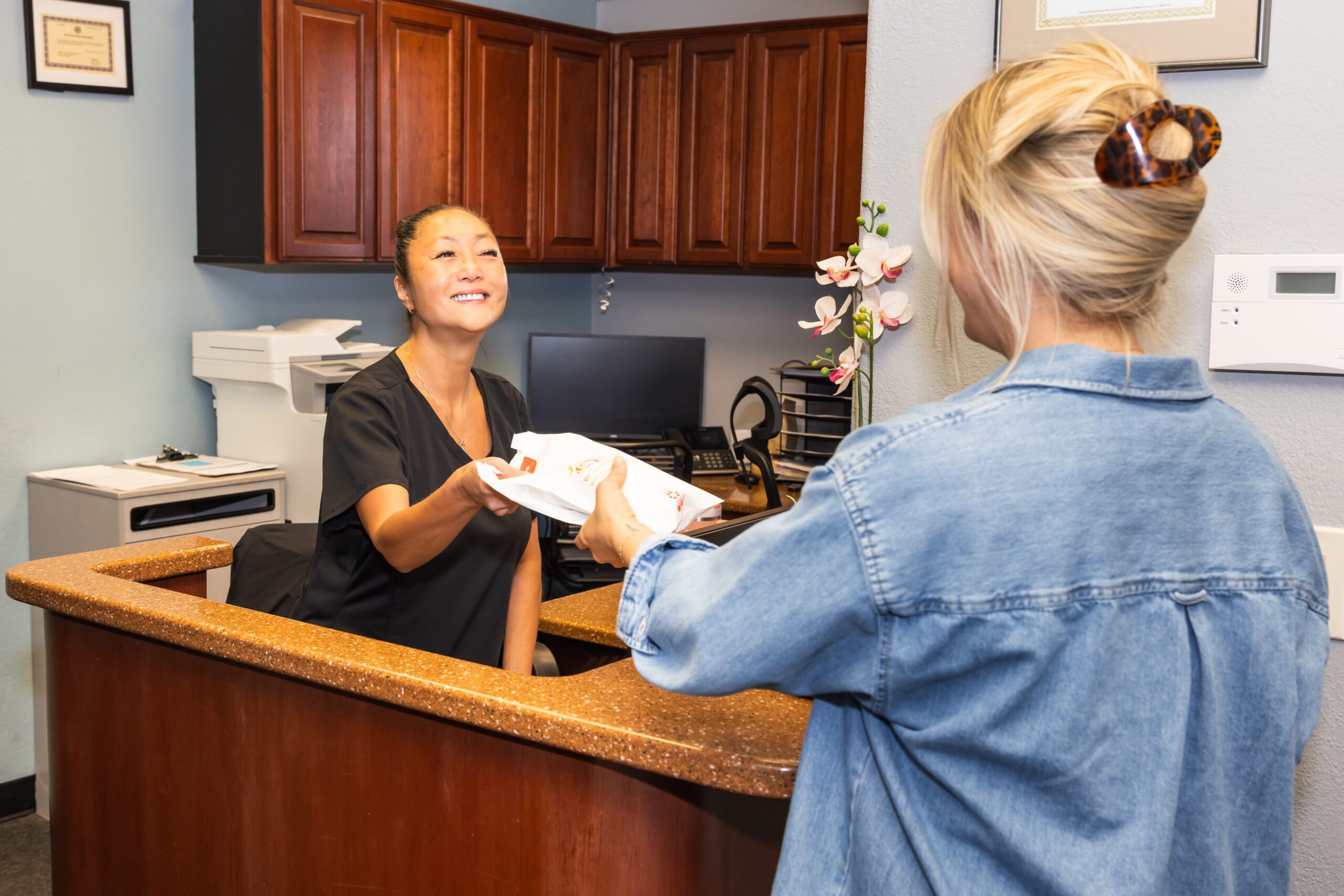 A dental staff hands paperwork to a patient at a countertop.